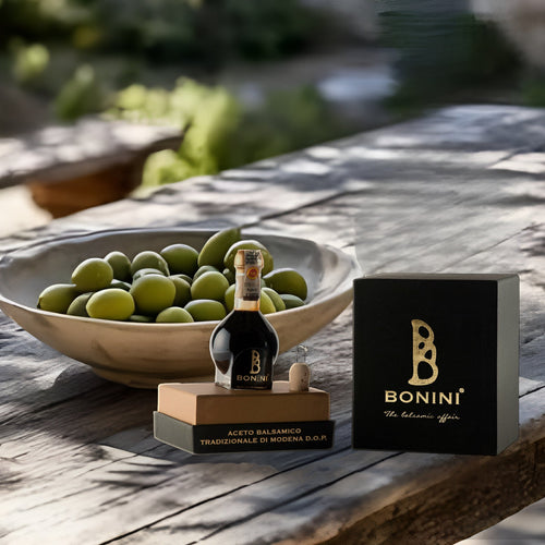 Aceto Balsamico Tradizionale di Modena DOP 25 ans, coffret noir Bonini, sur une table en bois sous les oliviers